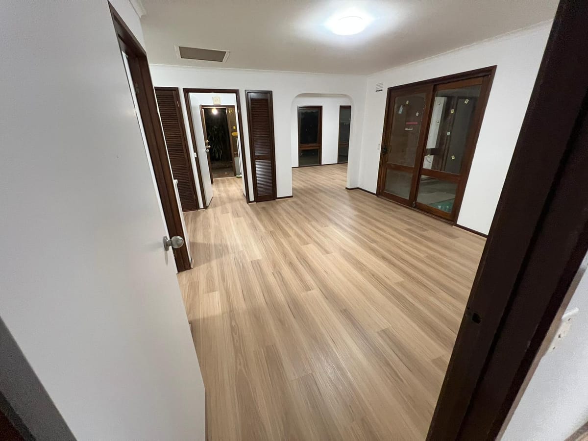 Sand Oak 1002 hybrid planks running through an open living area and hallway, framed by dark-stained doors and trim.
